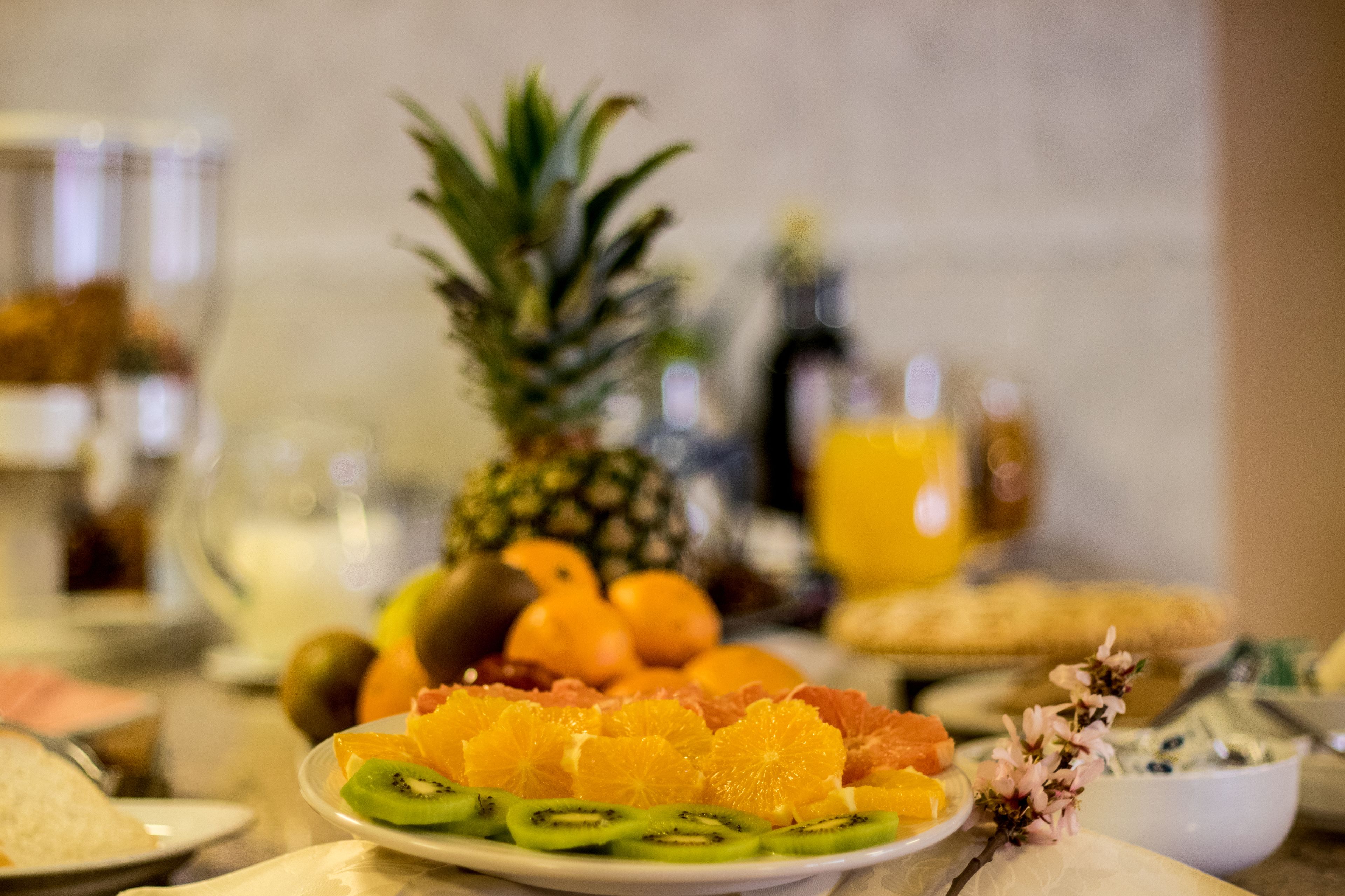 A breakfast table with various fruits, a pineapple, and a glass of orange juice.