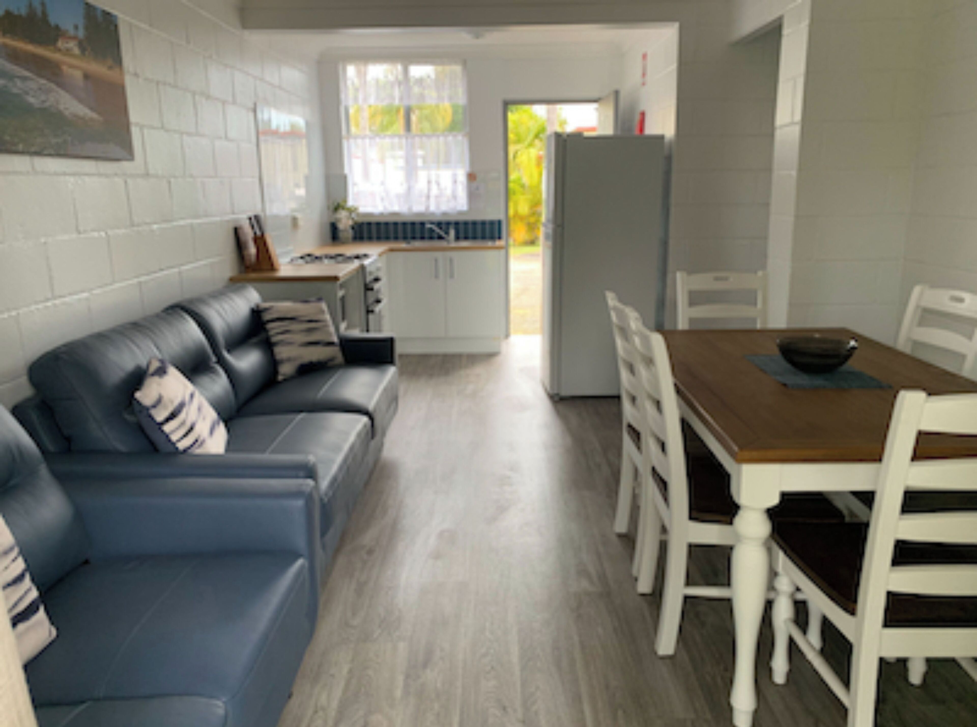 A modern kitchen with white cabinets, a dining table with chairs, and a blue leather sofa with pillows.
