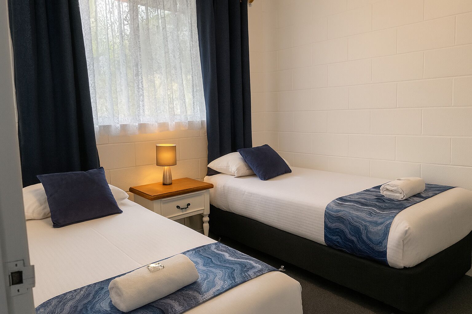 Een hotelkamer met twee bedden, een nachtkastje en een raam met gordijnen.