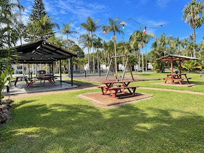 Un parque con mesas de picnic, un conjunto de columpios y un pabellón cubierto.