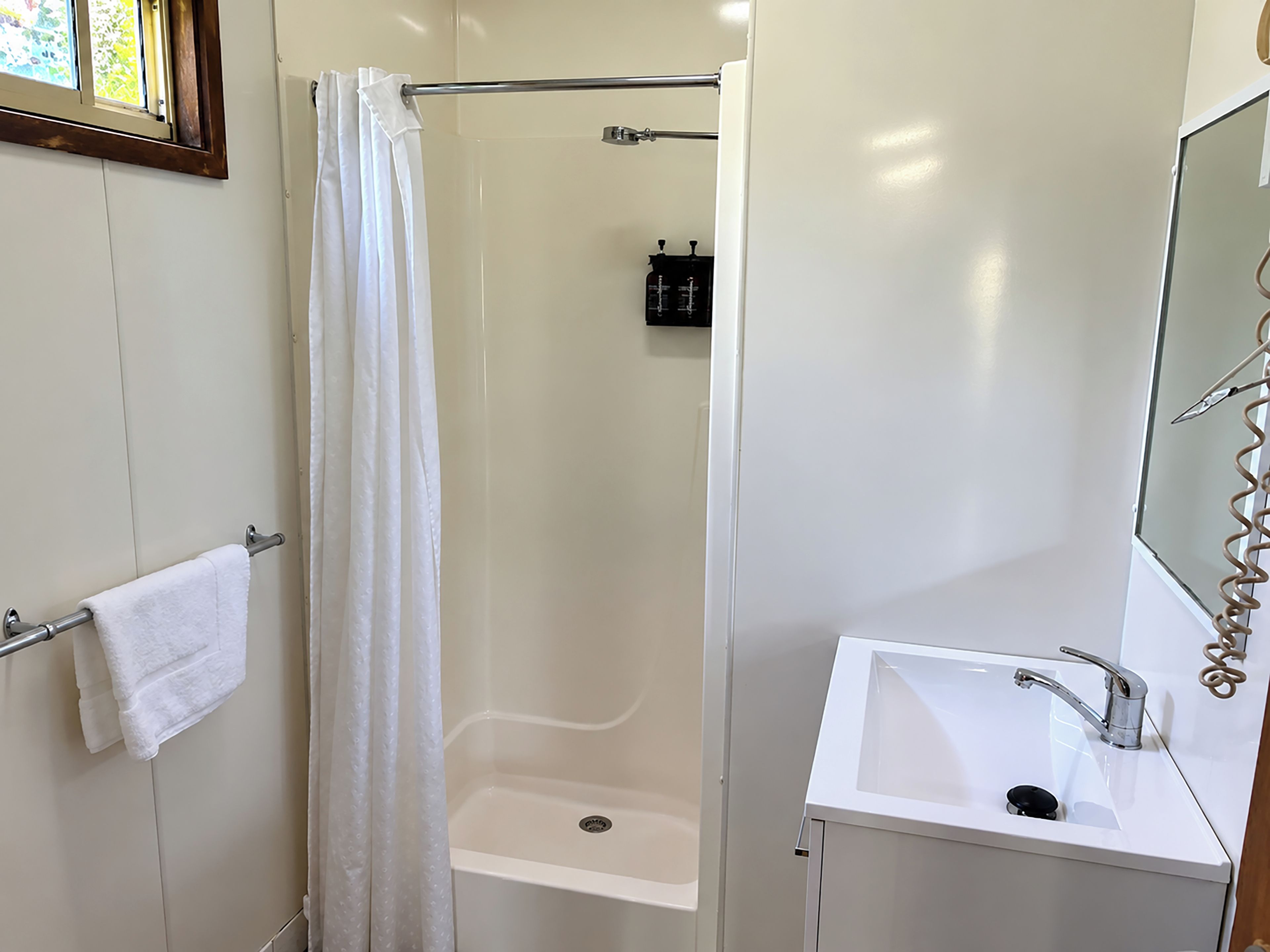 Un baño con ducha, lavamanos y espejo.