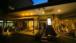 Edifici japonès tradicional amb un vestíbul cobert, fanals de pedra i una petita zona de jardí amb plantes en testos.