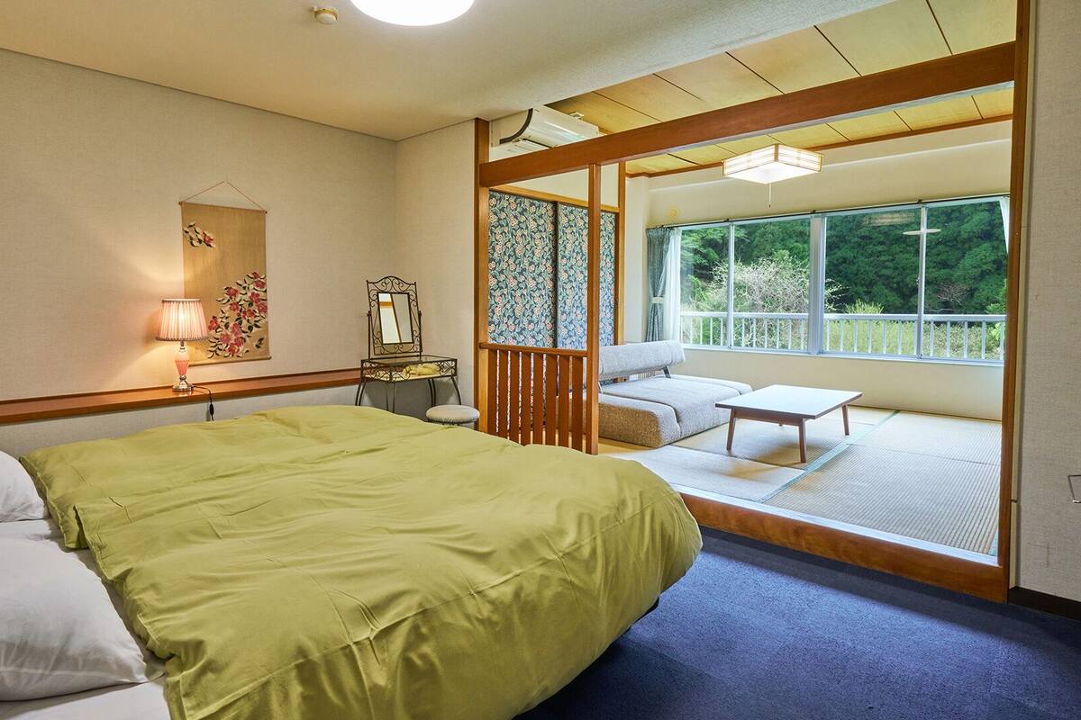 A room with a bed, a desk, a chair, a window, and a view of the outdoors.