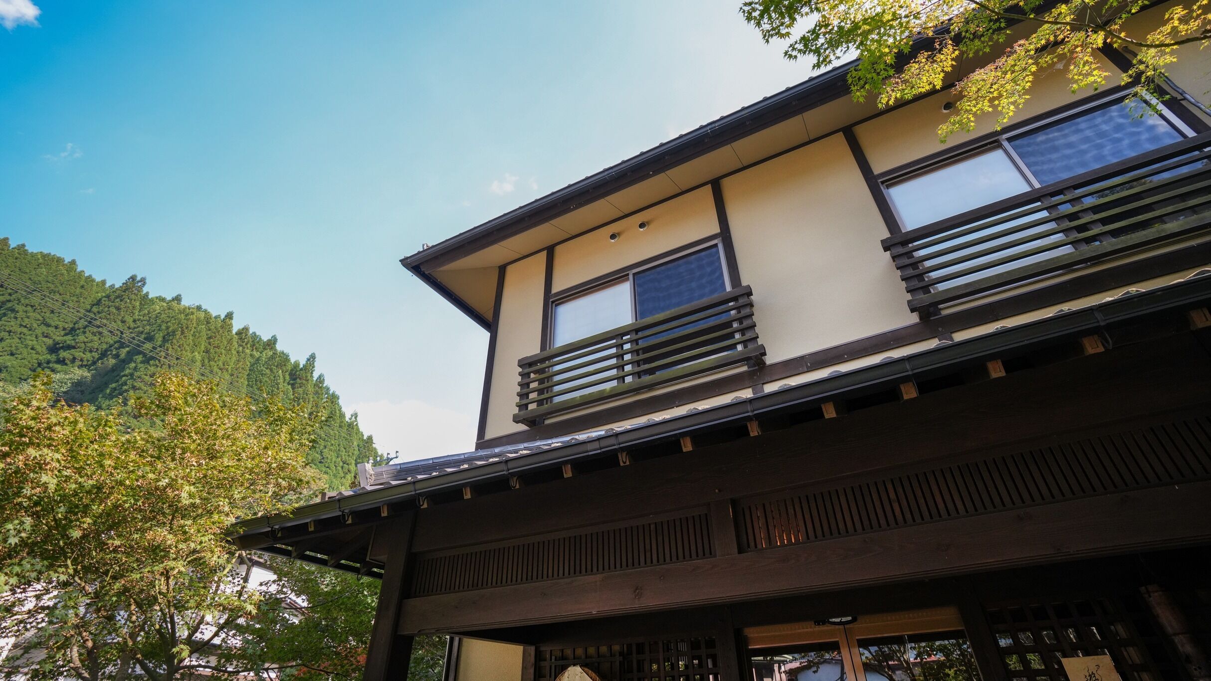 A traditional Japanese building with a wooden structure, large windows, and a view of a forested hillside.