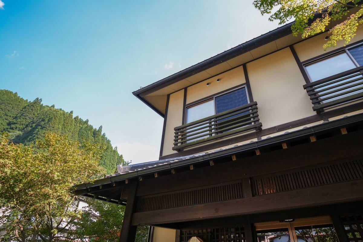 A traditional Japanese building with a wooden structure, large windows, and a view of a forested hillside.