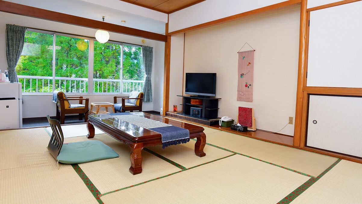 A traditional Japanese room with tatami flooring, a low table, chairs, a television, and a sliding door.