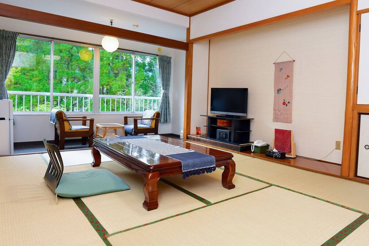 A traditional Japanese room with tatami flooring, a low table, chairs, a television, and a sliding door.