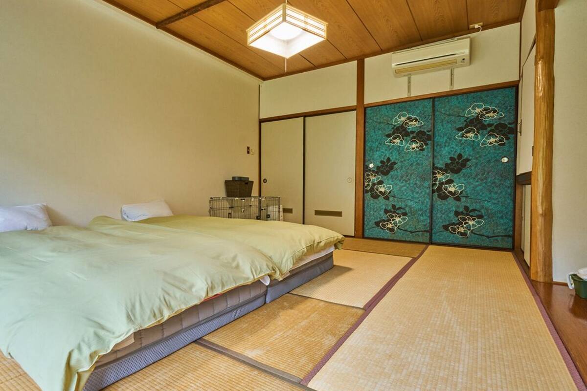 A traditional Japanese room with tatami flooring, a low bed, sliding doors with floral designs, and a ceiling light fixture.