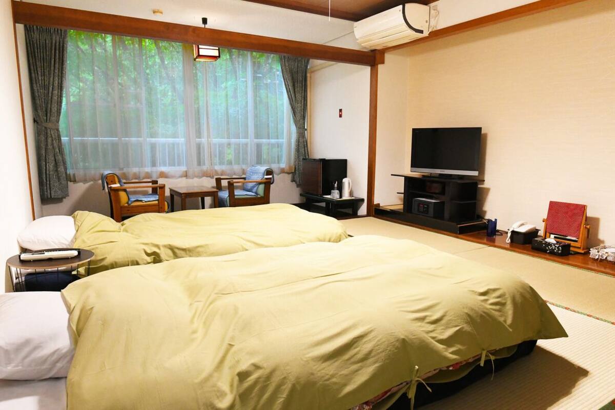 A hotel room with two beds, a TV, a desk with a chair, and a window with curtains.