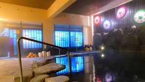 Una piscina interior amb escales de pedra que descendeixen a l'aigua, envoltada per parets amb finestres i decoracions circulars i de colors.