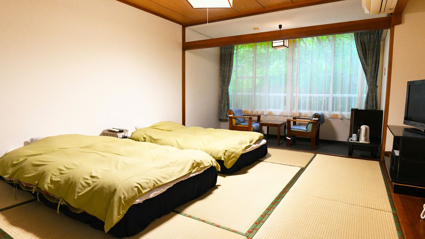 A room with two beds, a TV, a desk, and a window with curtains.