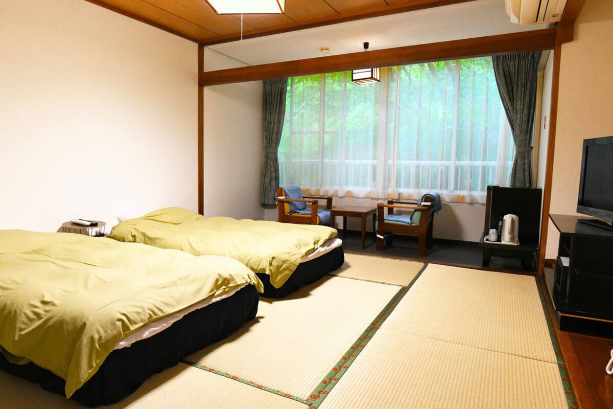 A room with two beds, a TV, a desk, and a window with curtains.