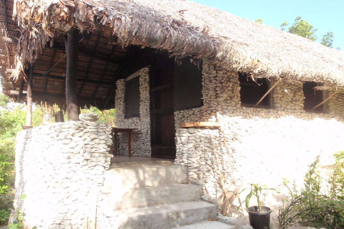A stone building with a thatched roof, a wooden door, and a small table outside.