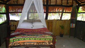 A bed with a canopy, a potted plant, and a bookshelf in a room with a thatched roof. - Tranquility Island Resort (Moso Island)