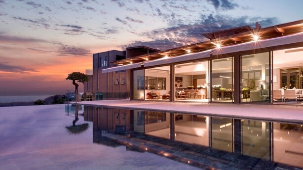 A modern house with a large glass facade, a pool, and a tree in the background. - Tropical Castle Layan by RESAVA (Choeng Thale)