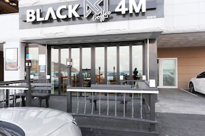 The exterior of a Black Coffee 4M establishment with a modern design, featuring large windows and a seating area visible through the glass.