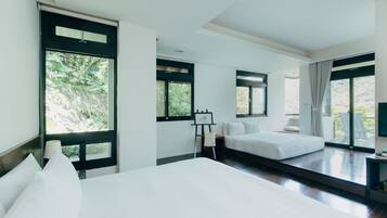 A modern hotel room with a large bed, a smaller bed, and a desk with a chair. There are large windows providing views of the outdoors.