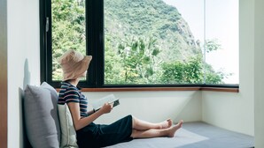 A person sitting on a bench by a window with a view of a mountain and greenery. - Adagio Jinguashi (New Taipei City)