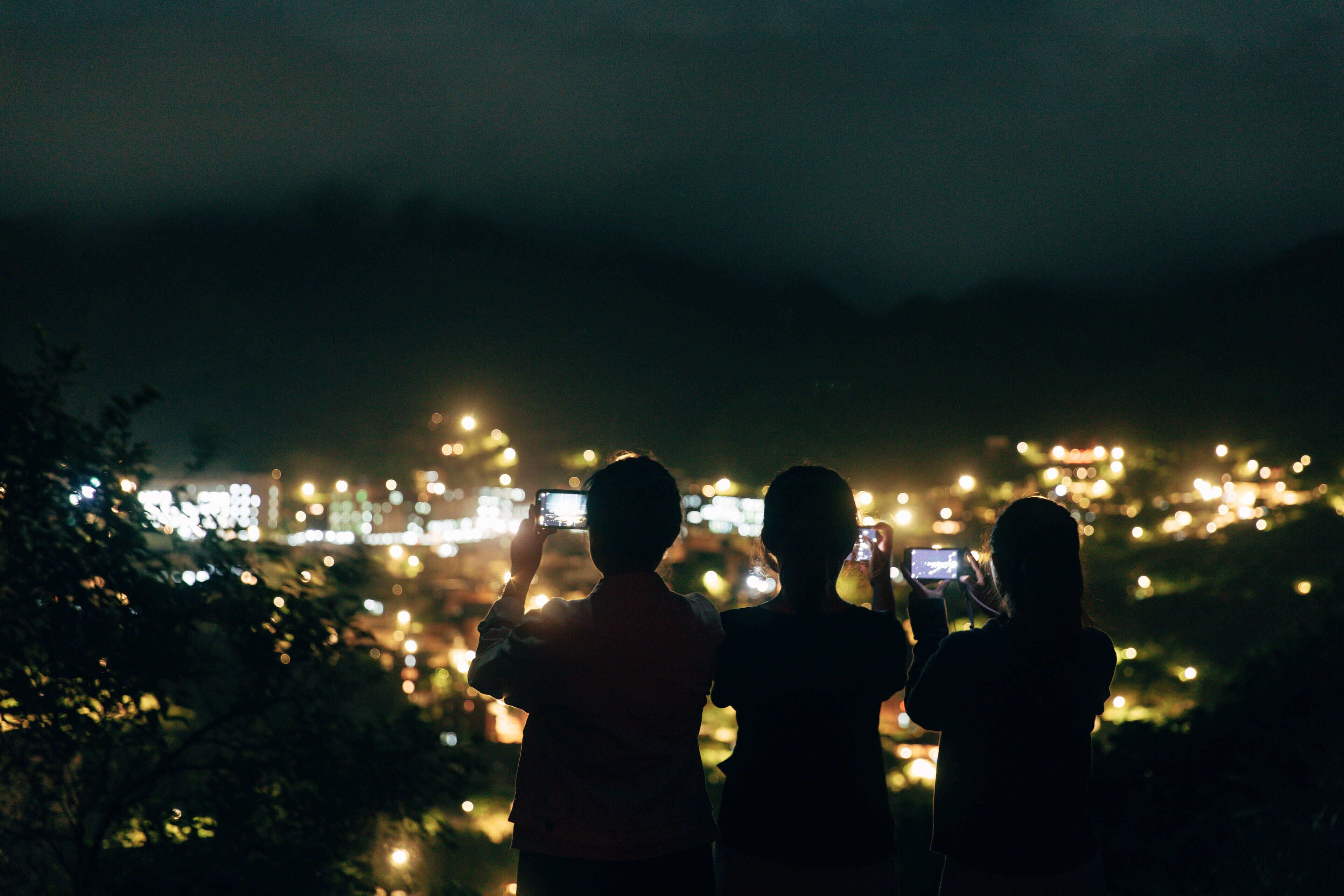 Silhouettes of people taking photos with a cityscape in the background.