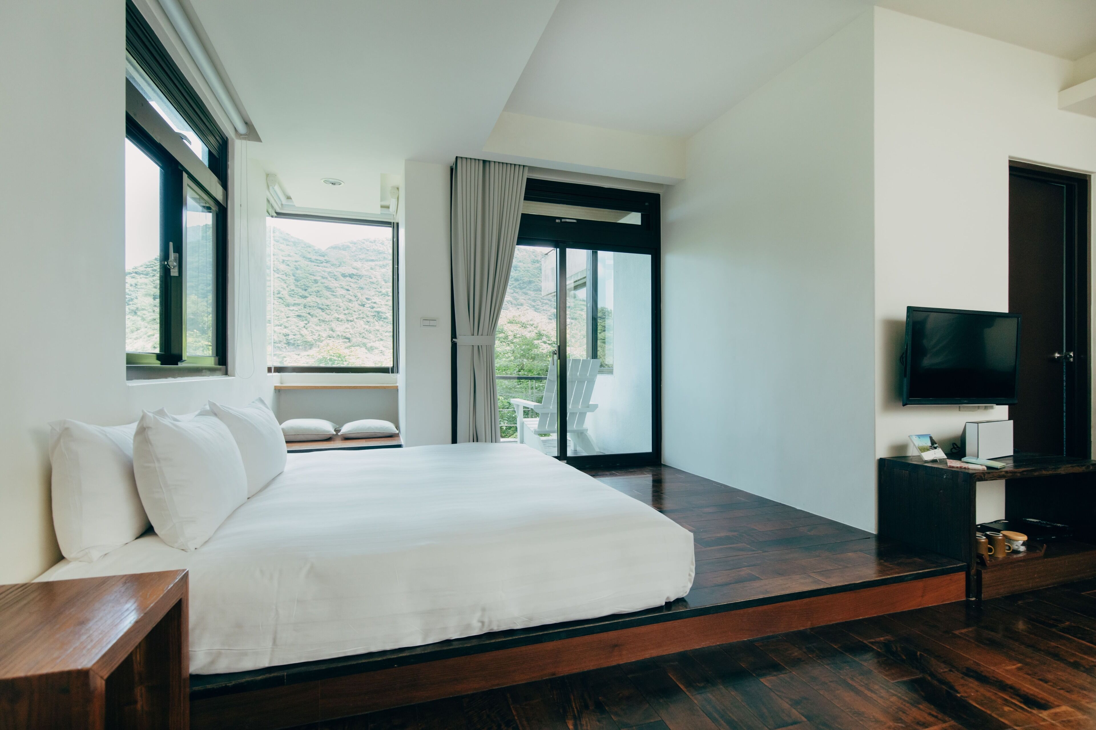 A modern bedroom with a large bed, a TV, and a balcony with a view of the mountains.