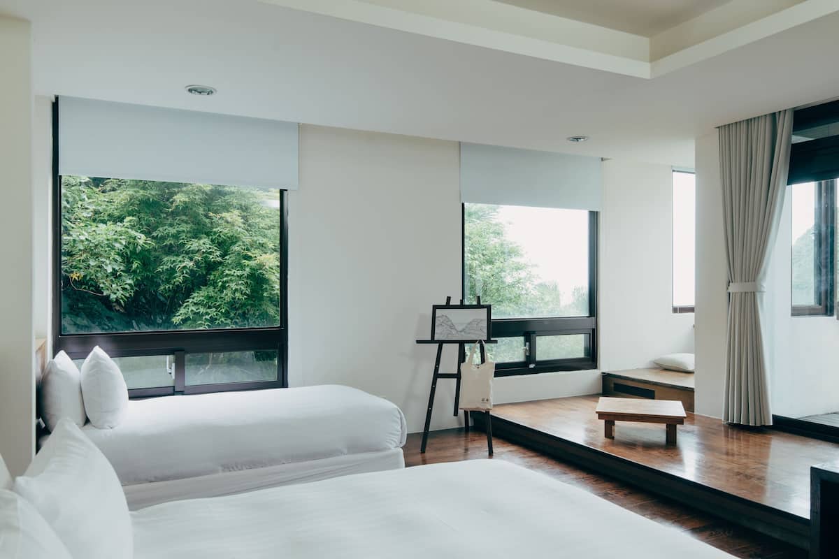 Habitación de hotel moderna con ventanas amplias, una cama, una mesita y un caballete con una pintura.