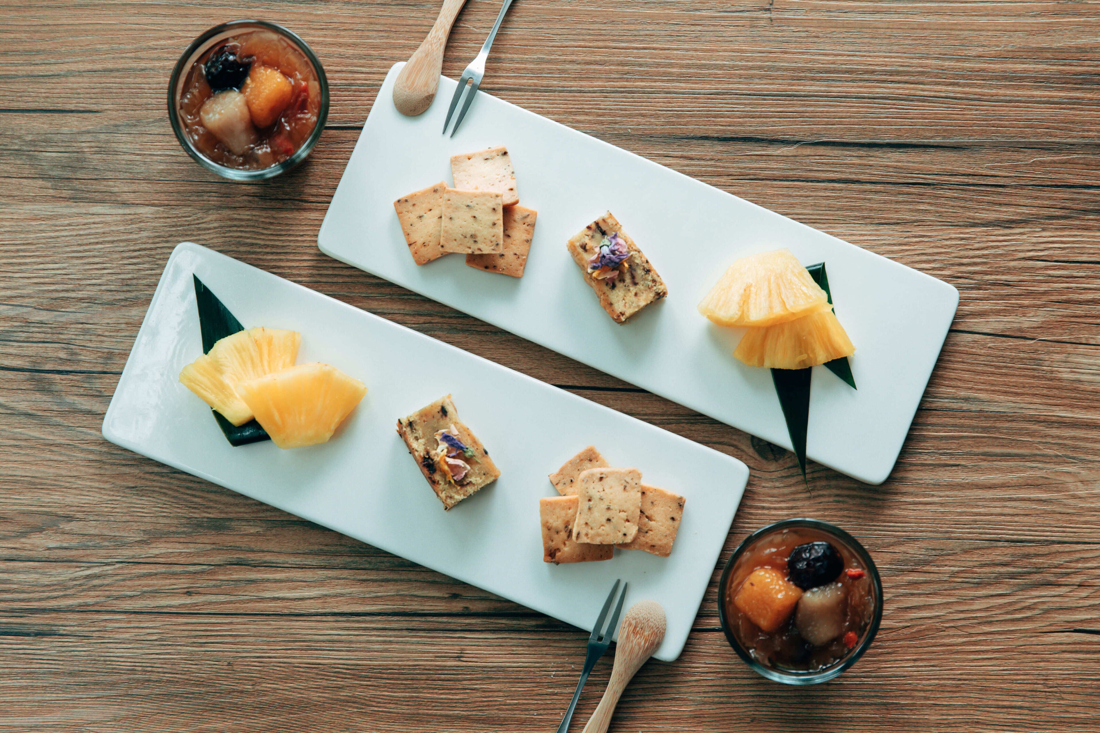 A wooden table with two rectangular white plates containing various food items and two forks.