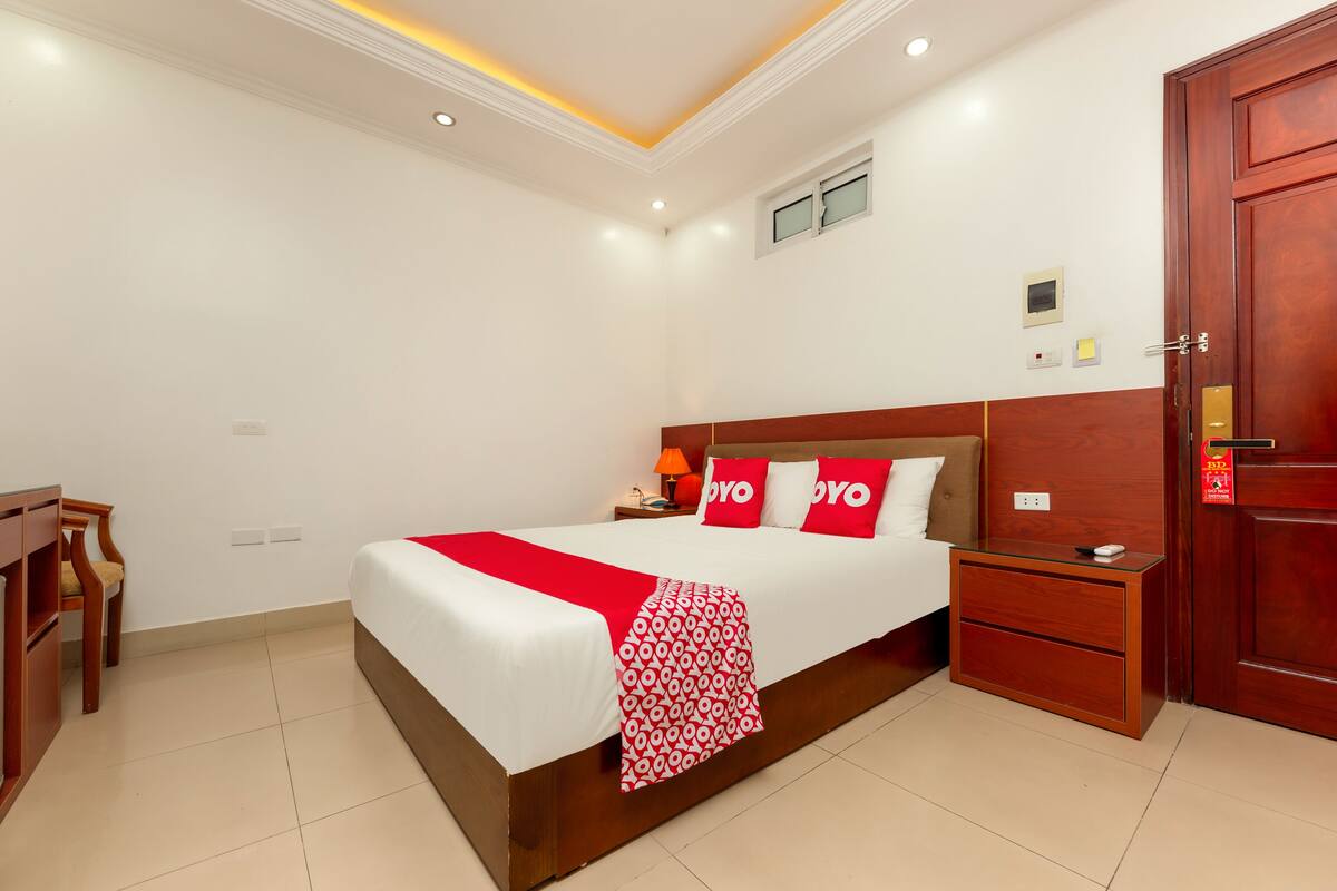 Una habitación de hotel con una cama grande, una mesita de noche de madera, un escritorio y un armario.