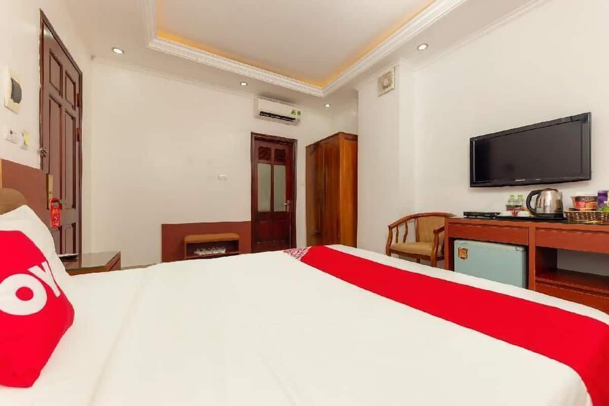 Habitación de hotel con cama, escritorio con televisor, armario y un pequeño mueble.