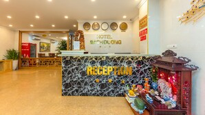 Zona de recepción de un hotel, con mostrador de mármol, relojes y un farol decorativo.