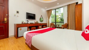 Habitación de hotel con cama, escritorio, televisor, refrigerador pequeño y ventana con cortinas.
