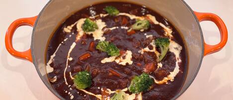 A pot of dark soup with broccoli and cheese on a table.