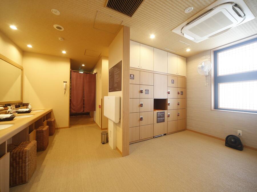 A hotel bathroom with multiple sinks, lockers, and a large window providing natural light.
