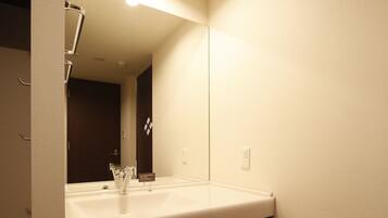 A compact hotel bathroom with a sink, mirror, and a small refrigerator.