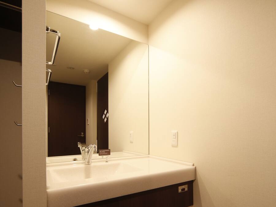 A compact hotel bathroom with a sink, mirror, and a small refrigerator.