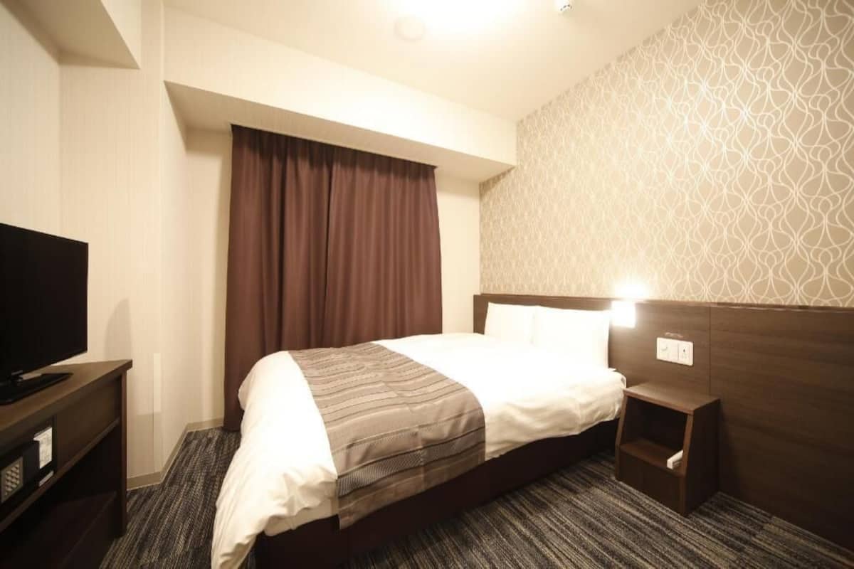 A hotel room with a bed, a television on a stand, a nightstand, and a patterned wall.