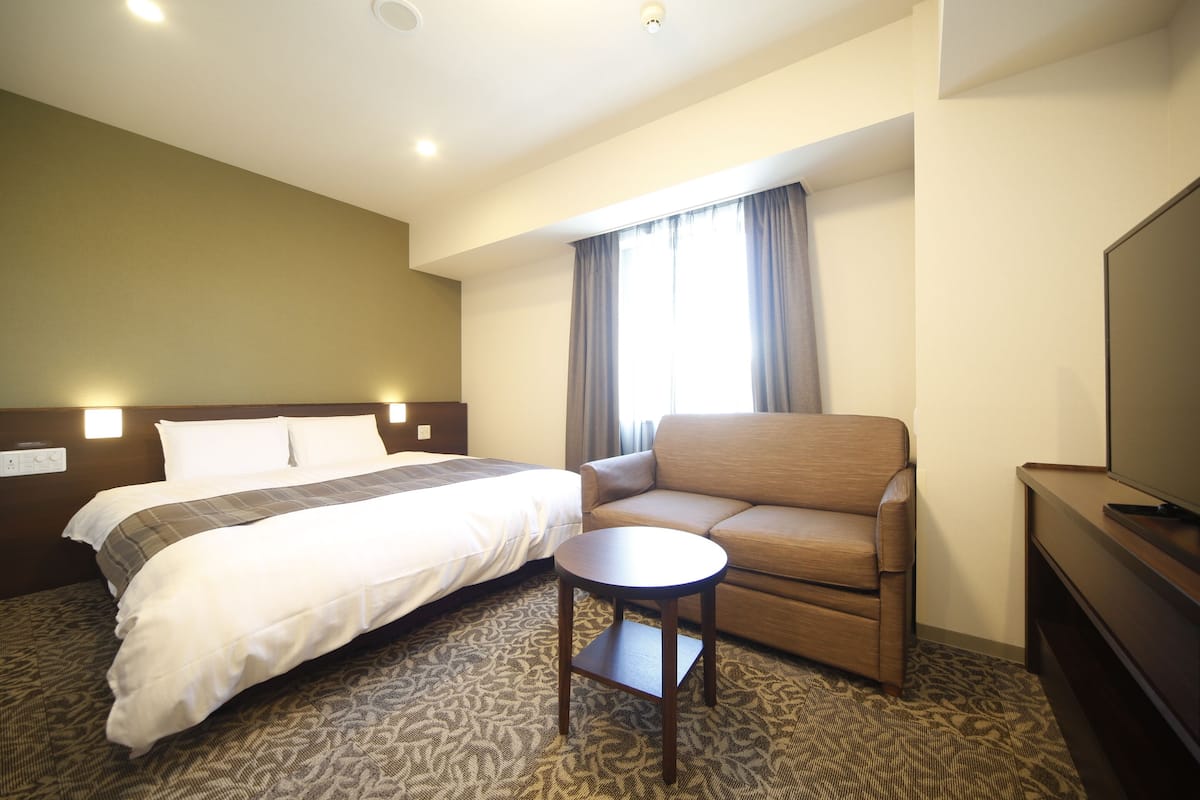 A hotel room with a bed, a sofa, a small table, and a TV.