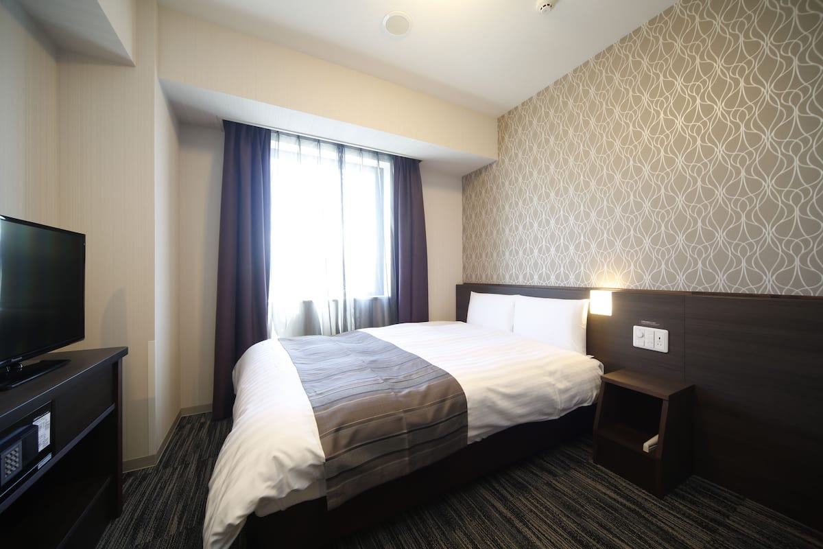 A hotel room with a large bed, a television, a bedside table, and a patterned wall.