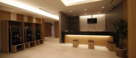 A modern hotel lobby with a reception desk, seating area, and a large plant.