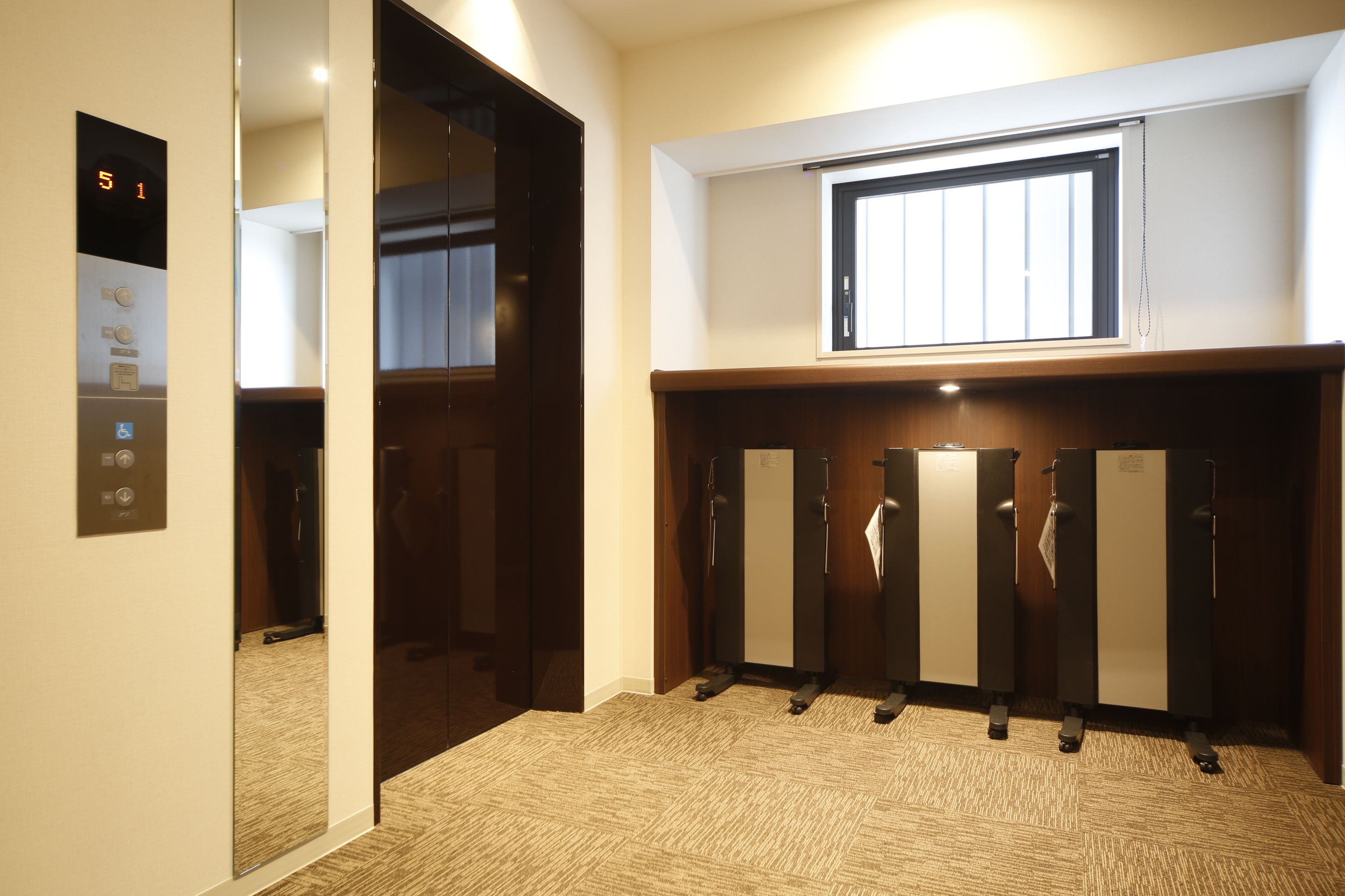 An elevator with a digital display showing '51', a mirror reflecting the elevator, and a row of lockers with a window above them.