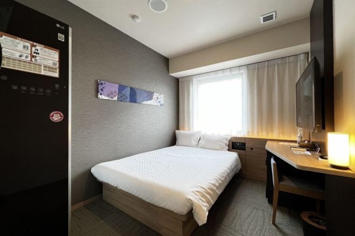 Une chambre d’hôtel avec un lit, un bureau, une télévision et une fenêtre avec des rideaux.