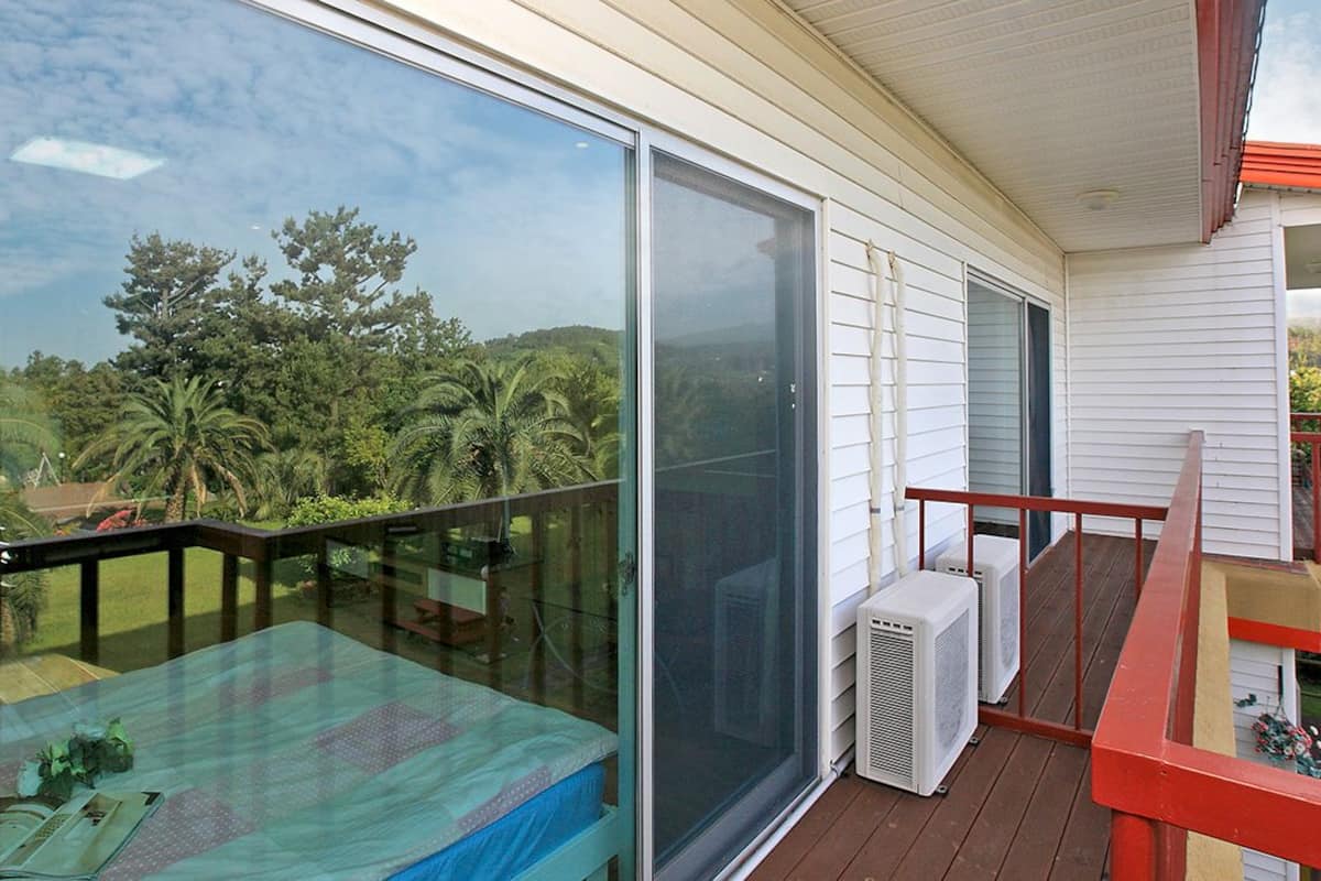 Un balcon doté d’une paroi vitrée, d’une rambarde rouge et d’un appareil de climatisation.