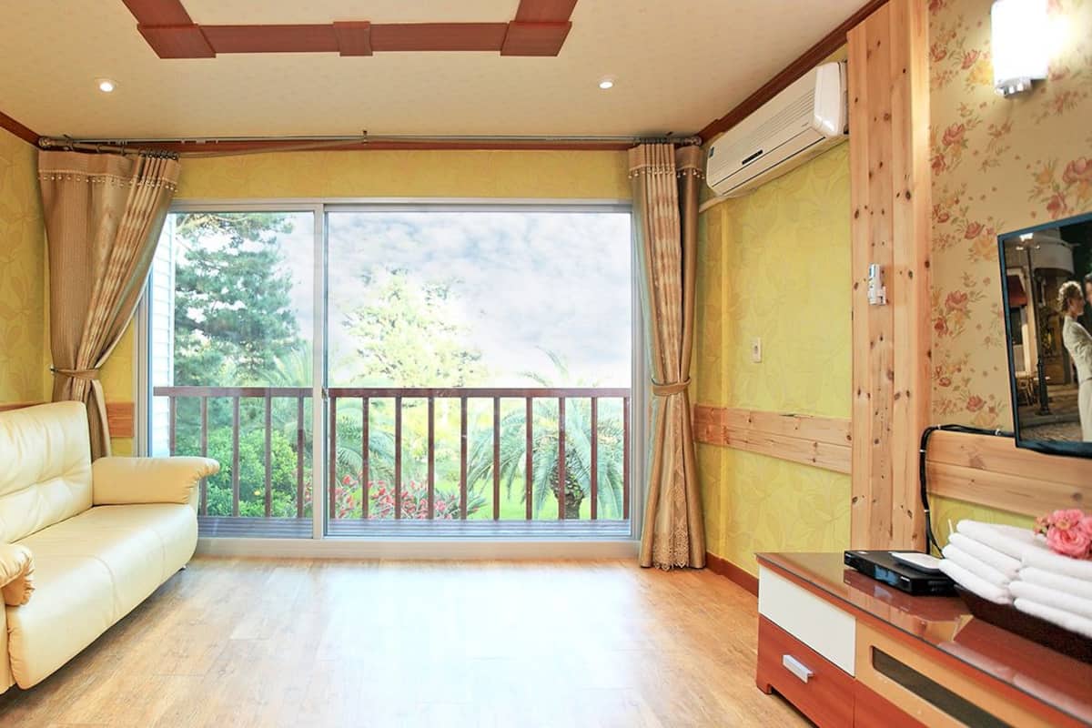 Une pièce spacieuse avec un canapé beige, un bureau en bois avec un ordinateur et une grande fenêtre donnant sur un balcon.