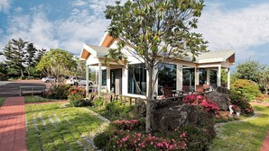A modern house with a covered patio, surrounded by a landscaped garden with rocks and flowering plants. - The Areumdaun Pension (Seogwipo)