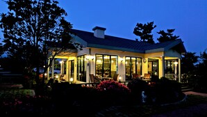 A two-story building with a covered patio area, large windows, and outdoor seating. - The Areumdaun Pension (Seogwipo)