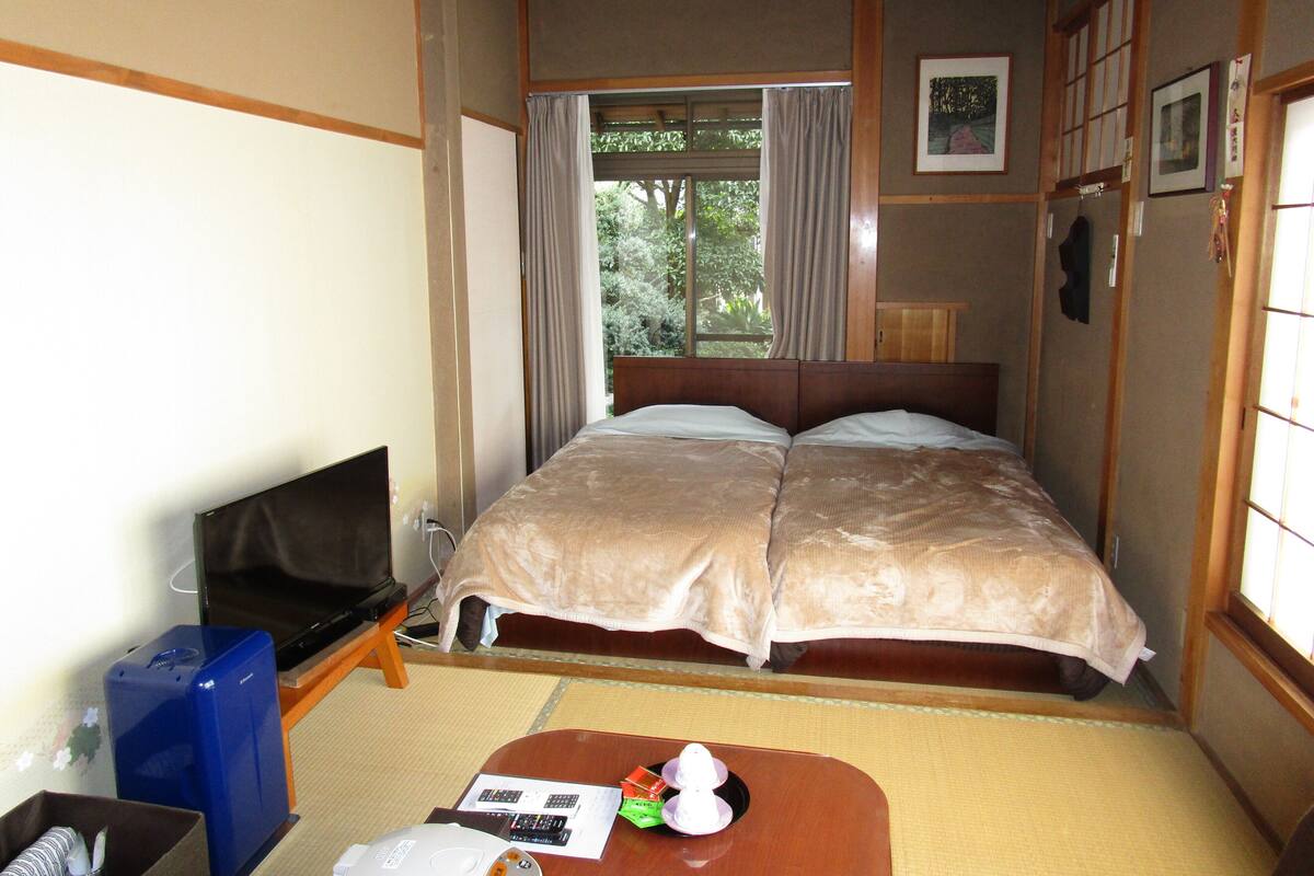 Quarto de hotel com uma cama, televisão, escrivaninha e janela com cortinas.