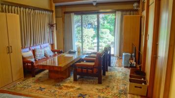 A cozy living room with a sofa, chairs, a coffee table, and a TV. There is a large window with curtains, a door, and a patterned rug.