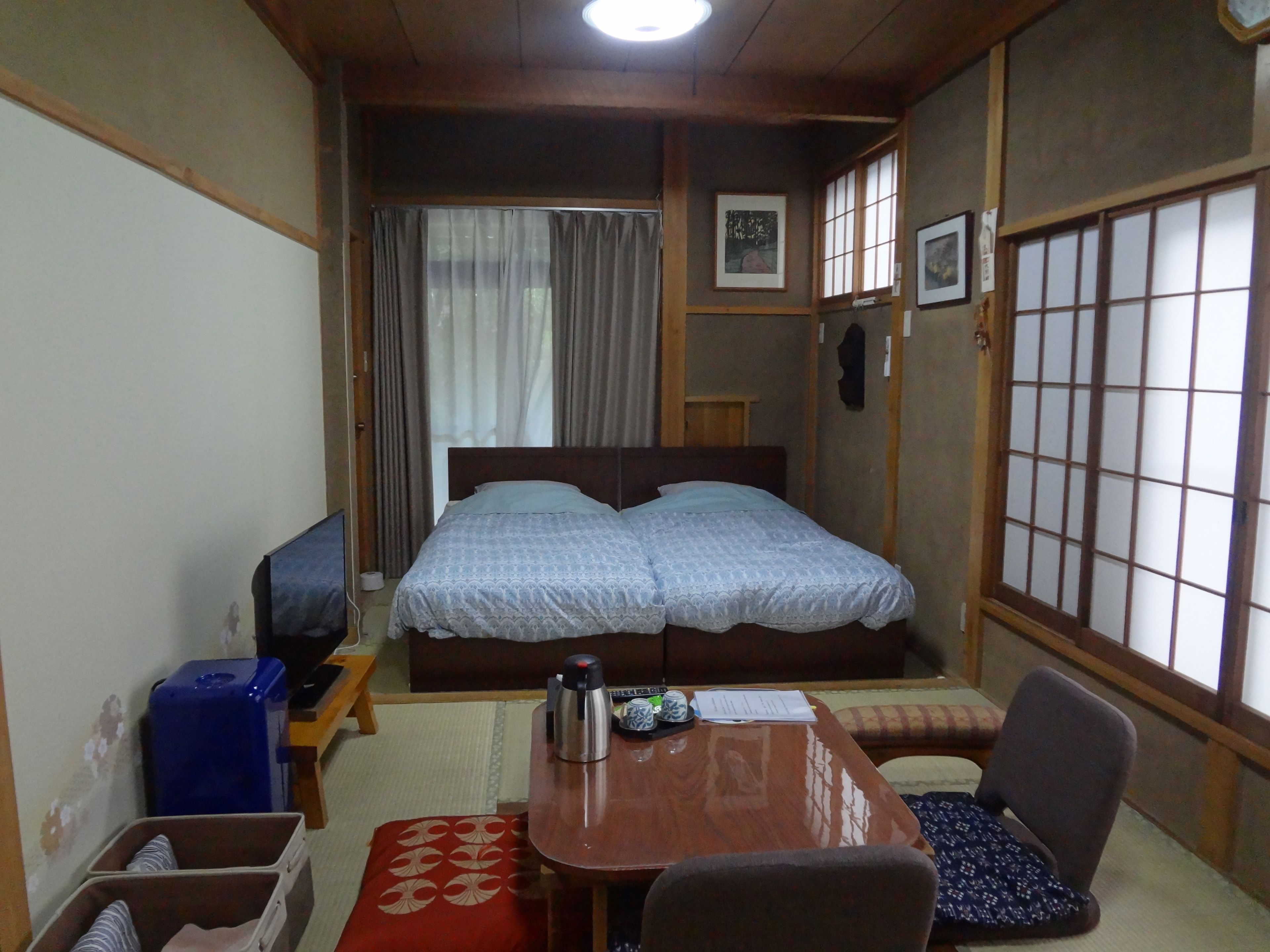A traditional Japanese-style room with a bed, a wooden table, a chair, and a futon.