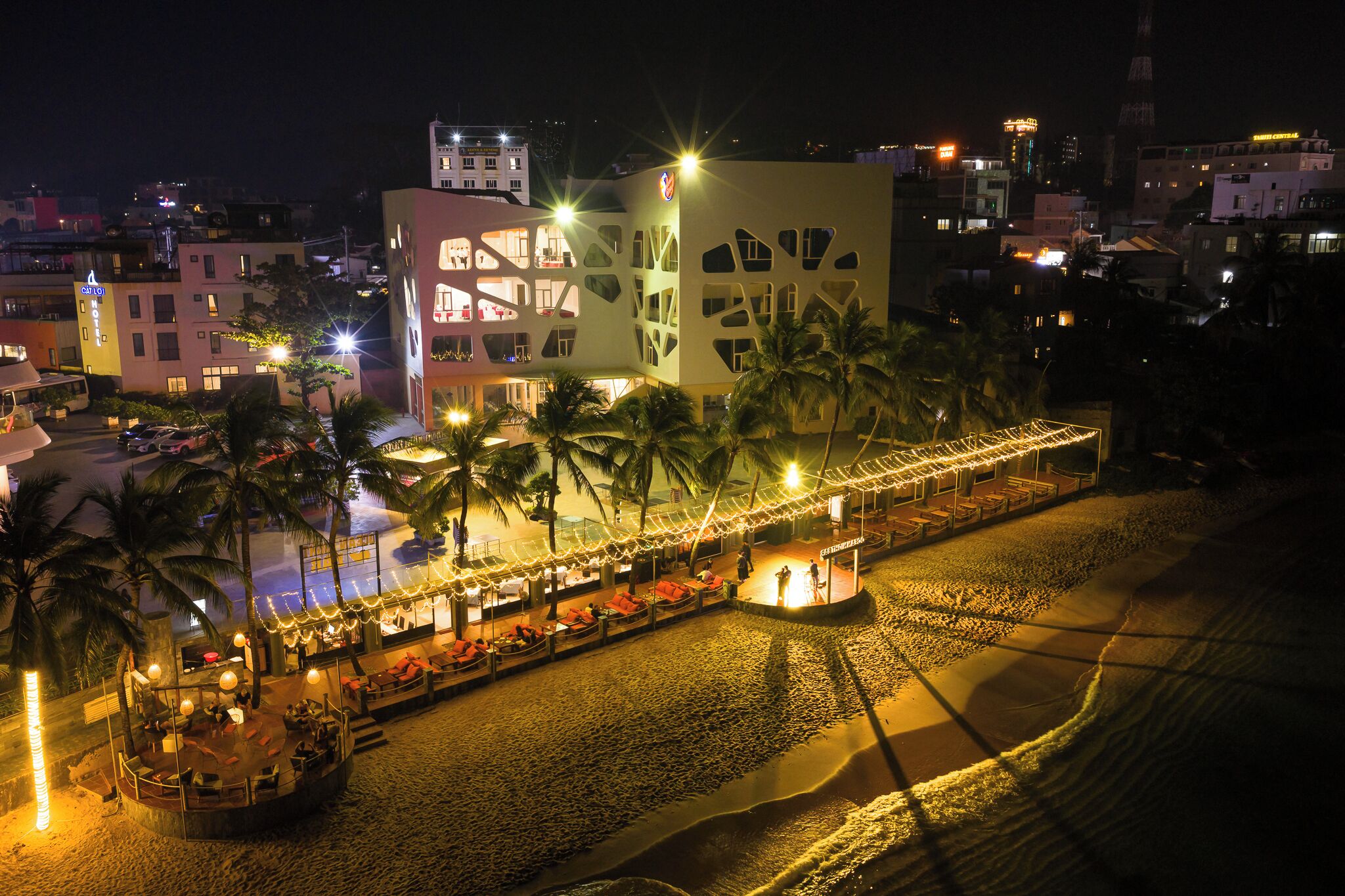 A beachfront hotel with a pool area, palm trees, and a covered walkway.
