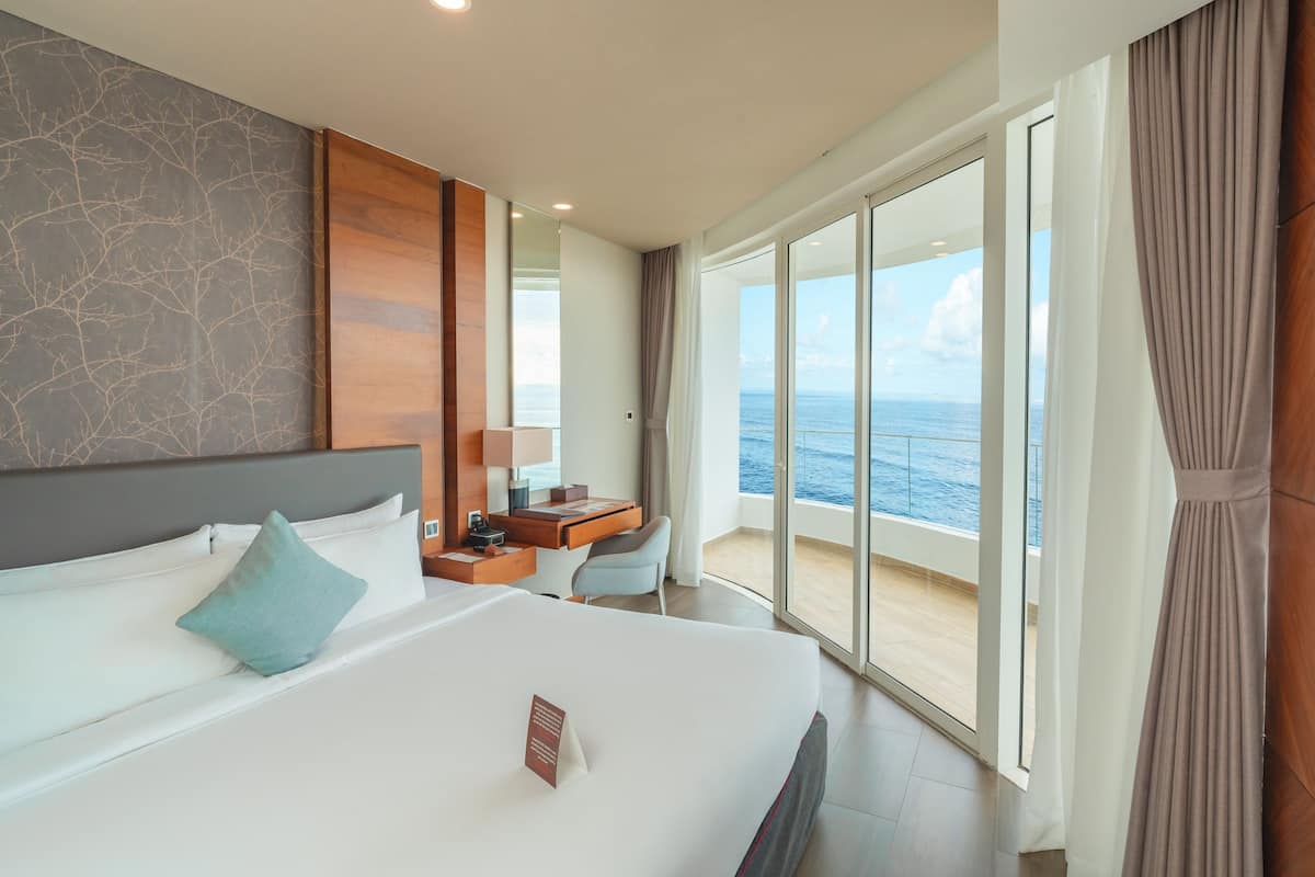 A modern hotel room with a large bed, a desk, and a view of the ocean.