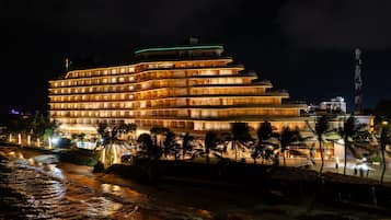 A multi-story hotel with a modern design, located near a beach with palm trees and a view of the ocean.